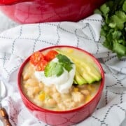Red bowl filled with cooked chicken chili and avocados, tomatoes, and cilantro on top.