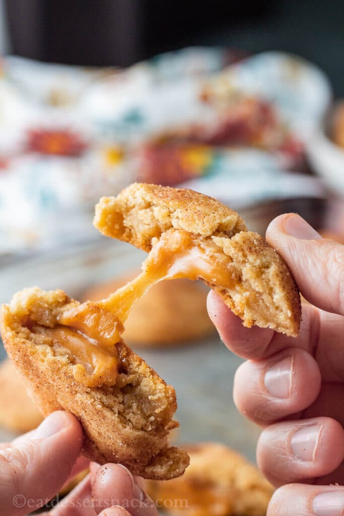 hands pulling caramel stuffed cookie apart with caramel in middle. 
