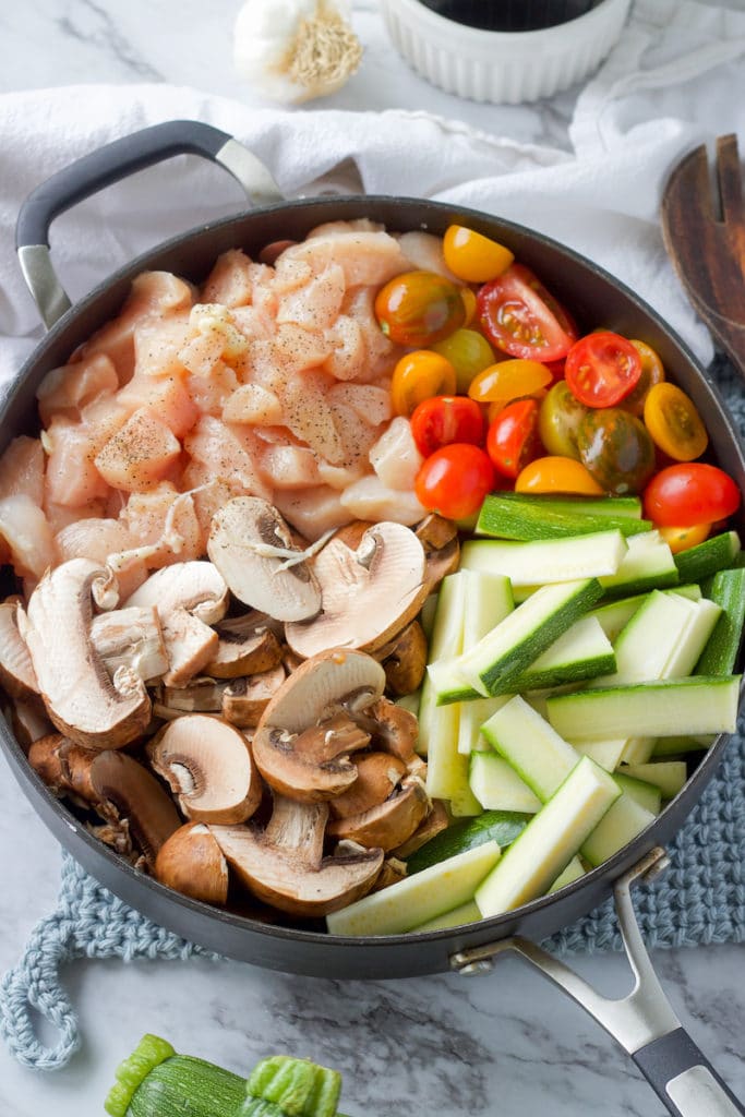 Raw chicken, tomatoes, zucchini, and mushroms in a killet. 