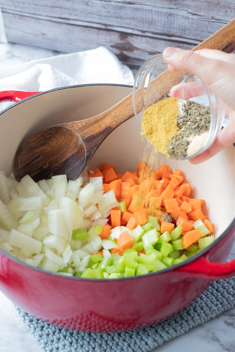 Spices being poured into a large pot of Carrots, Onion, and celery. 