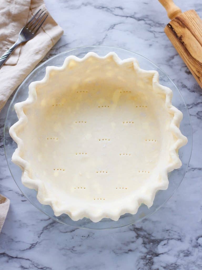 Raw cream cheese pie dough in glass pan with crimped edges. 