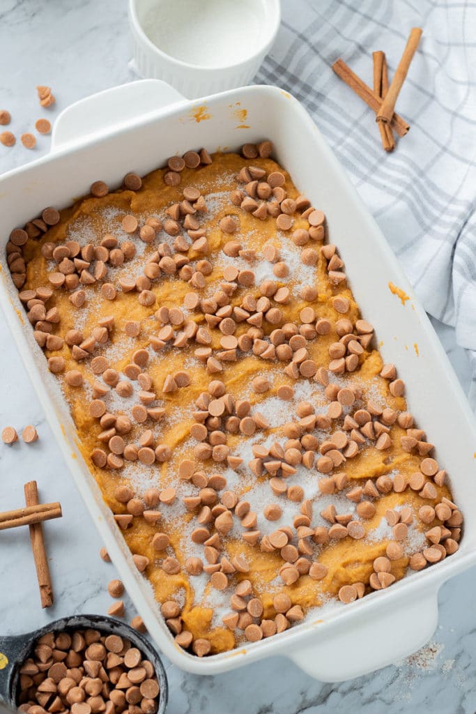 Raw Pumpkin Butterscotch Cake batter in white pan with butterscotch chips and sugar sprinkled on top. 