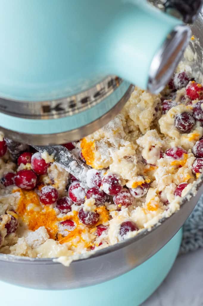Stand mixer with raw cake batter inside, with cranberries and orange zest. 