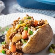Cooked Shepherd's pie filling inside a baked potato on white plate.
