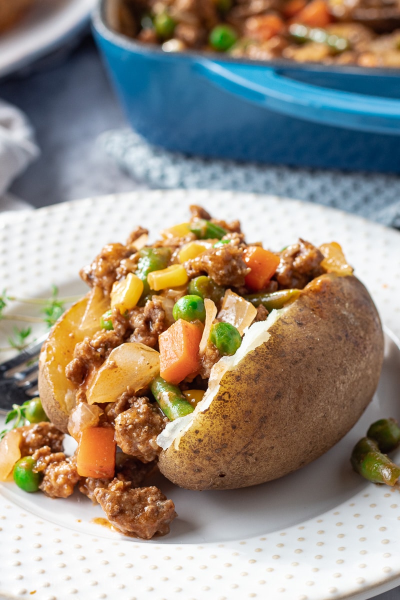 Cooked Shepherd's pie filling inside a baked potato on white plate. 