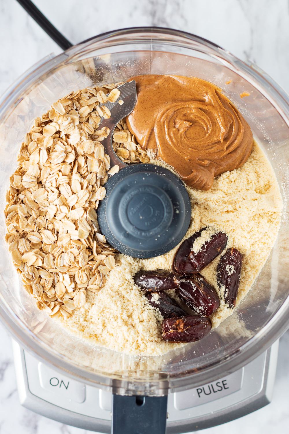 Regular oats, almond butter, almond flour, and dates in bowl of food processor. 