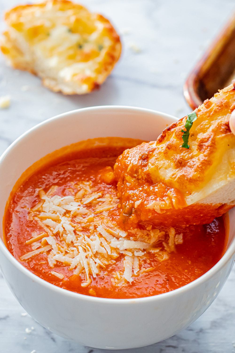 Cooked homemade tomato soup with cheese bread dipped in a white bowl.