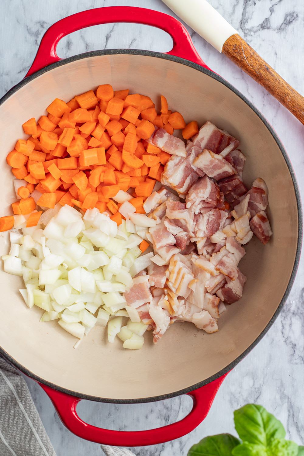 raw carrots, onions, and bacon in a red pot. 