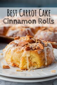 Baked carrot cake cinnamon roll with icing on white plates.