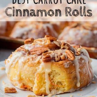 Baked carrot cake cinnamon roll with icing on white plates.