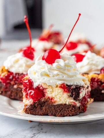 Slice of baked Cherry cheesecake brownie on white plate with whipped cream.