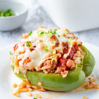 Cooked green pepper filled with ground beef, pinto beans, tomatoes, and cheese on top on a white plate.