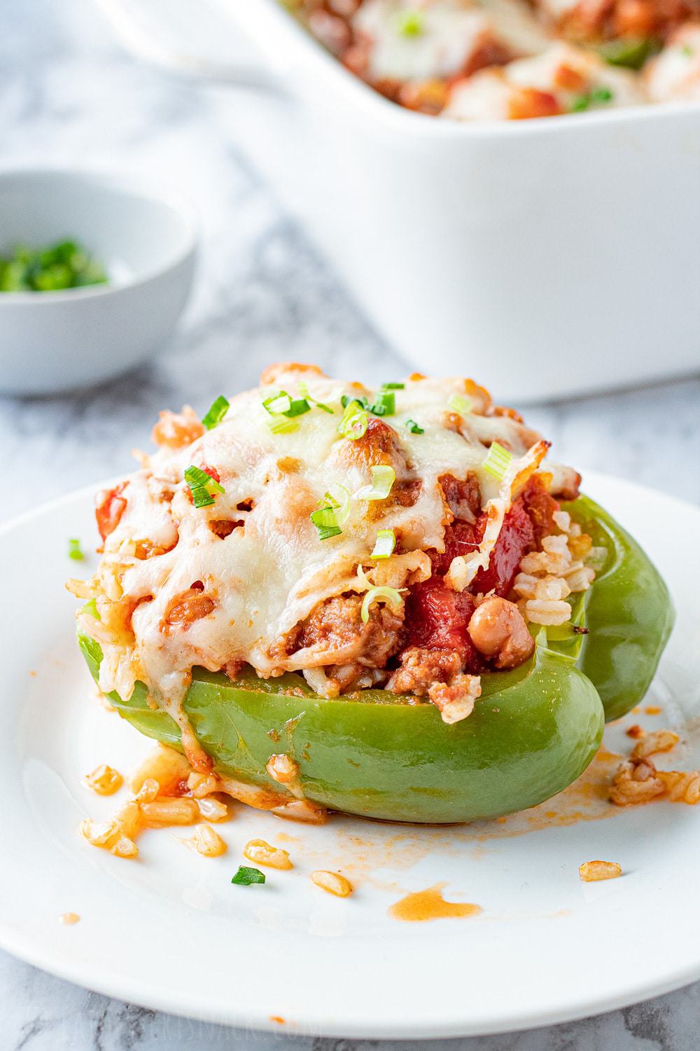 Cooked green pepper filled with ground beef, pinto beans, tomatoes, and cheese on top on a white plate.