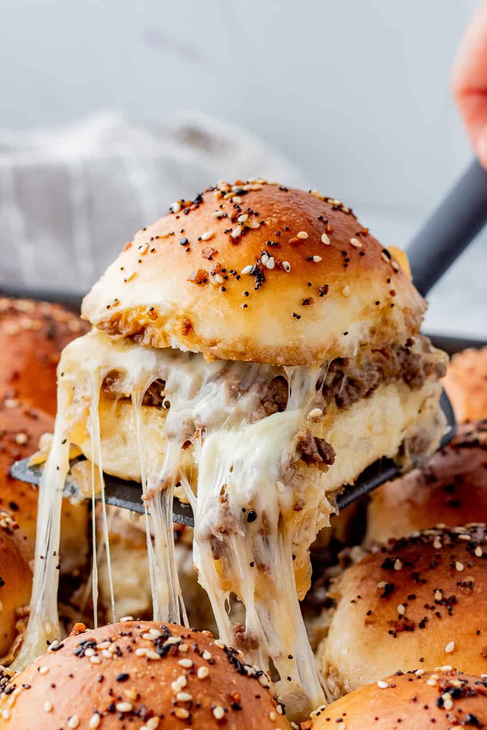 Dinner roll sliced in half with ground beef and caramelized onion filling with cheese on a black spatula.