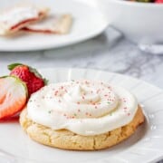 Baked strawberry poptart sugar cookie on a white plate with strawberries.