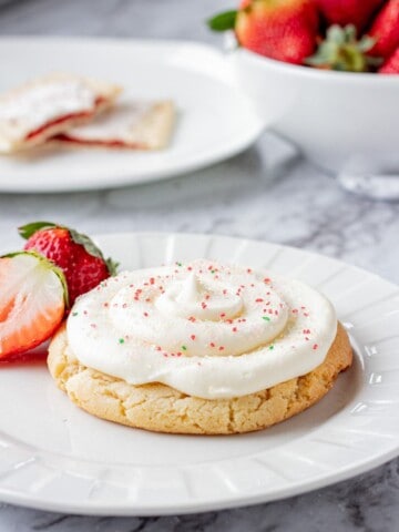 Baked strawberry poptart sugar cookie on a white plate with strawberries.