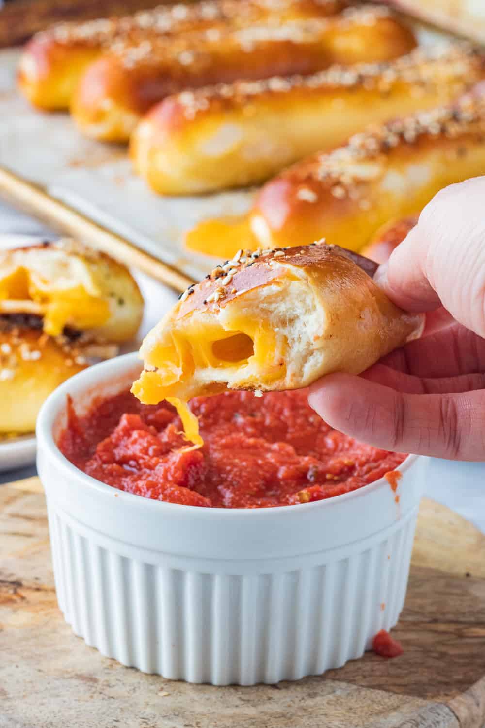 half of a baked cheese pretzel above white bowl of pizza sauce. 