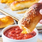 baked cheese pretzel above white bowl of pizza sauce.