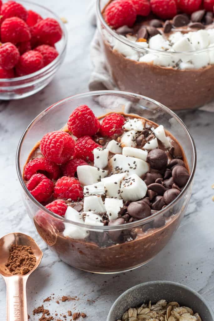 Glass bowl of chocolate overnight oats with coconut and raspberries.