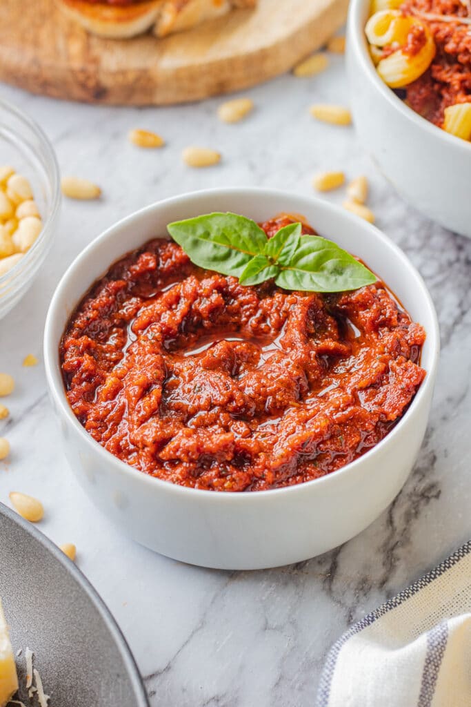 Red Pesto Sauce in white bowl with basil leaves