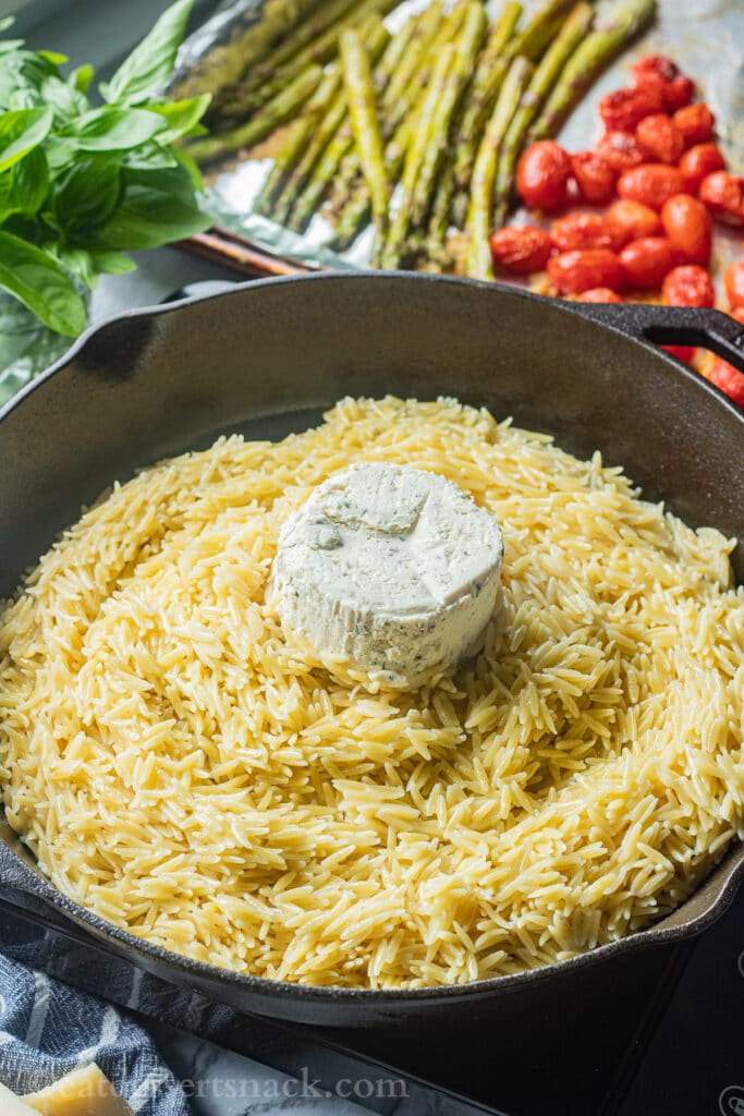 Cooked orzo in a pan with boursin cheese on top. 
