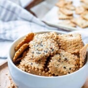 Sourdough crackers in white bowl on wood board.