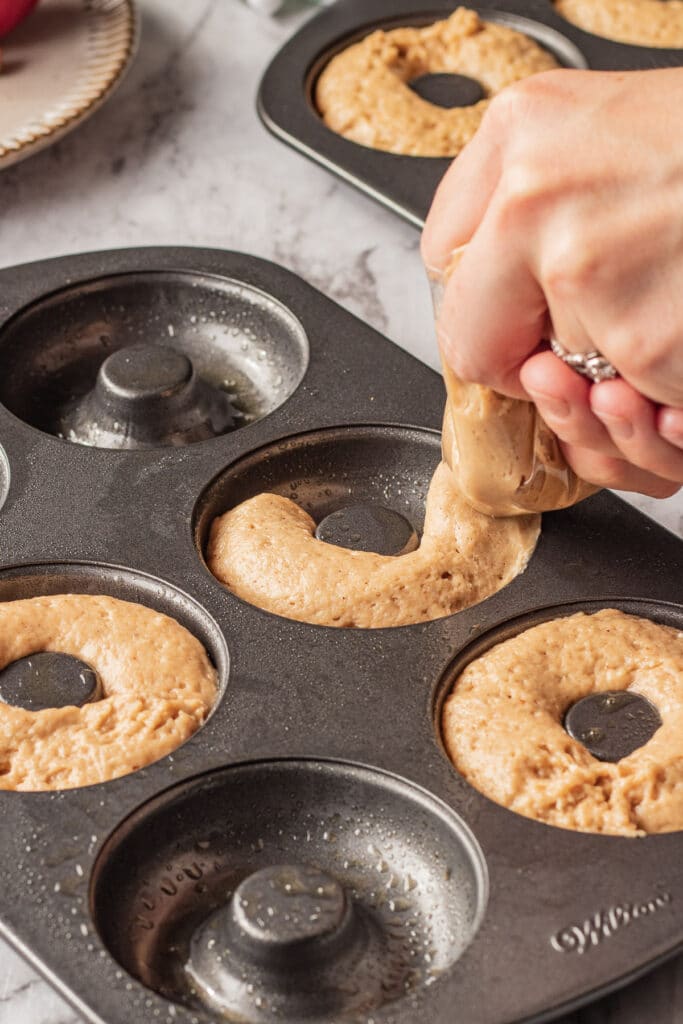 Apple cider donut batter being piped into a donut pan. 