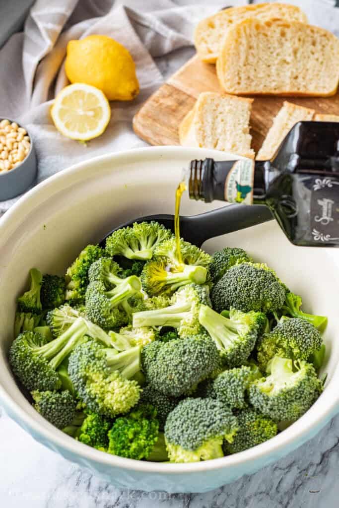 Pouring olive oil into bowl of raw broccoli. 
