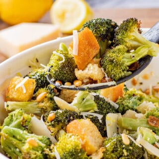 Spoonful of cooked roasted broccoli salad above blue bowl.