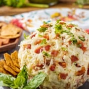 Bacon Pesto Cheeseball on black plate with basil and crackers.