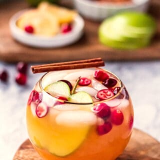 Round glass of apple cider punch on wood board with lemon slice.
