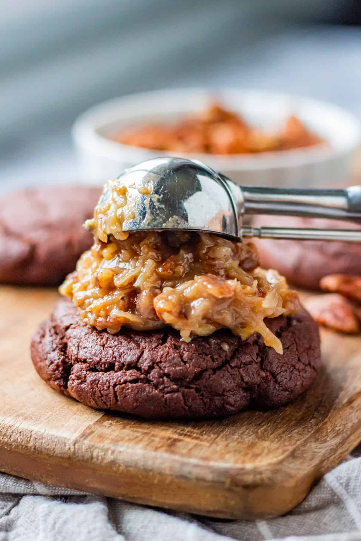 Scooping coconut pecan frosting onto baked chocolate cookie. 