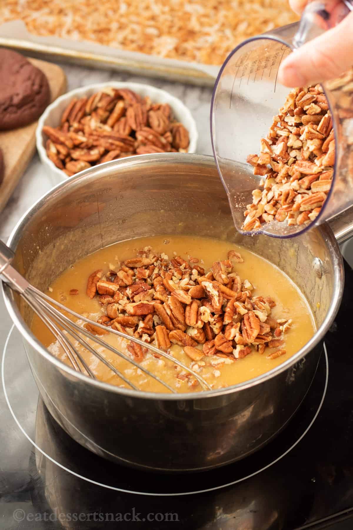 Pecans pouring into metal pan of butter brown sugar mixture. 