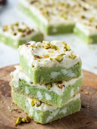 Stack of 3 frosted pistachio bars on wood board.