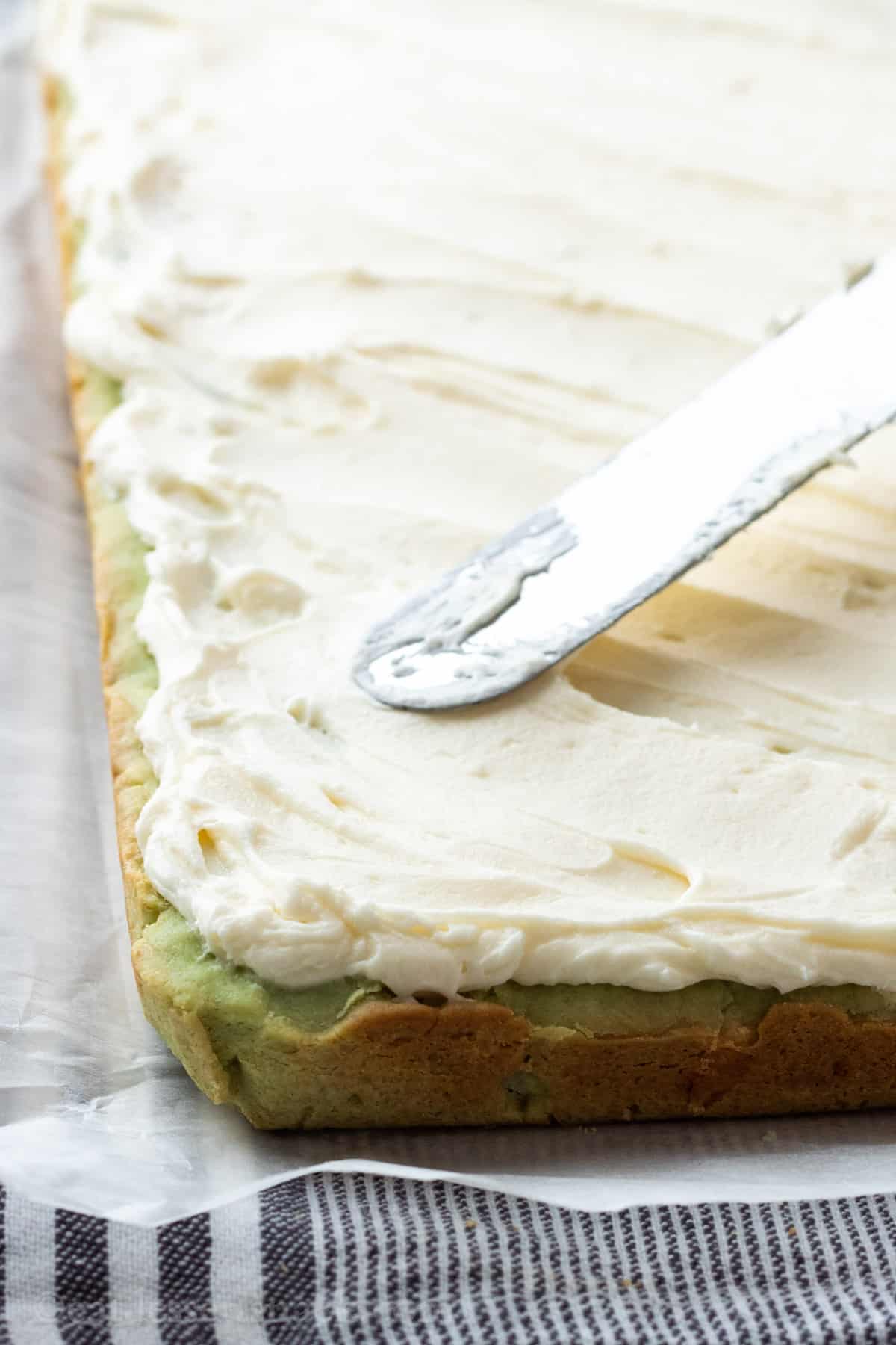 Spatula spreading frosting on baked pistachio bars. 