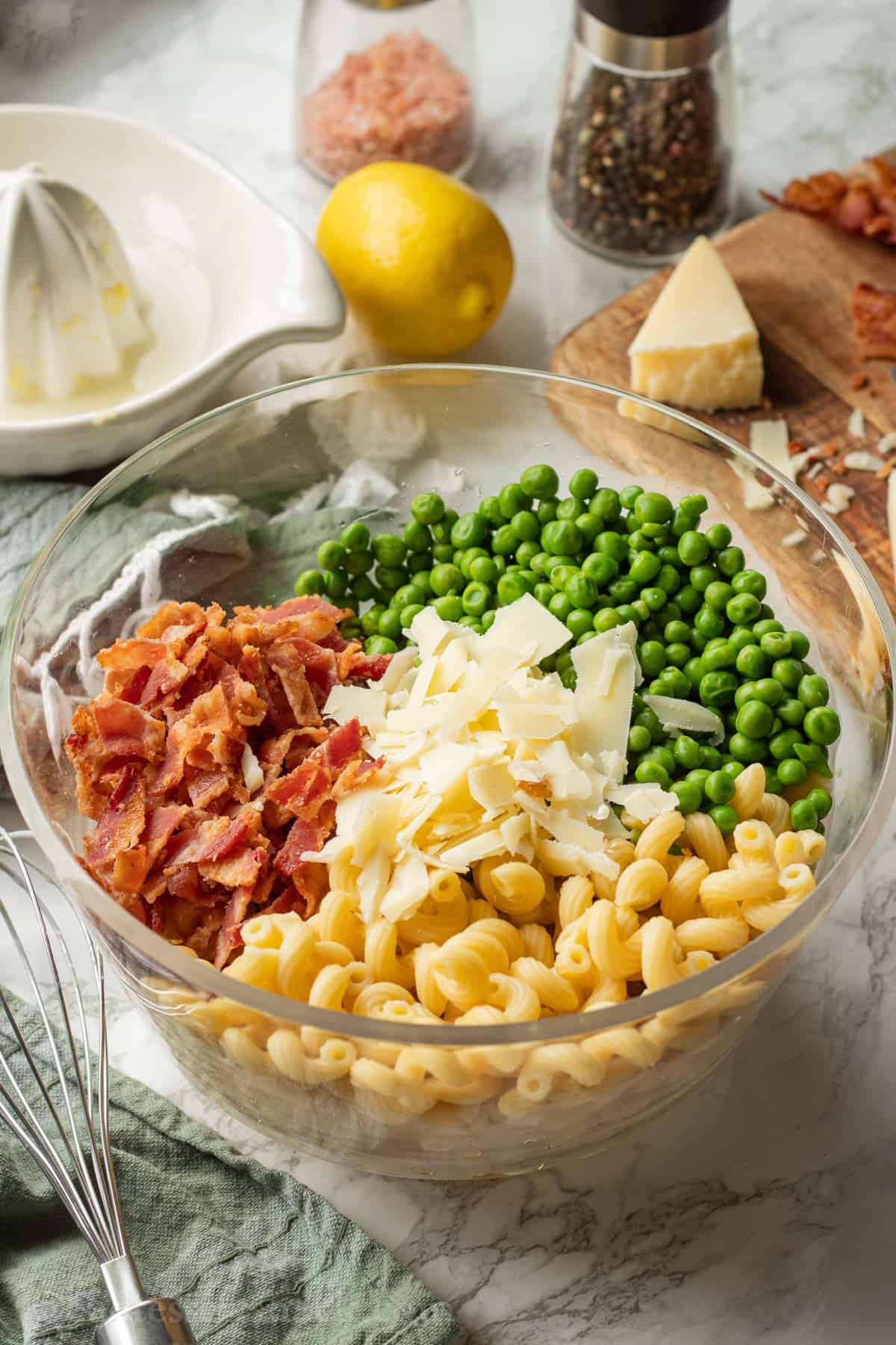 Bacon, peas, parmesan, and pasta in clear bowl on marble. 