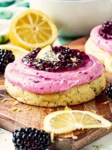 Baked Lemon Blackberry Cookie with frosting on wooden cutting board with lemon slices and blackberries.