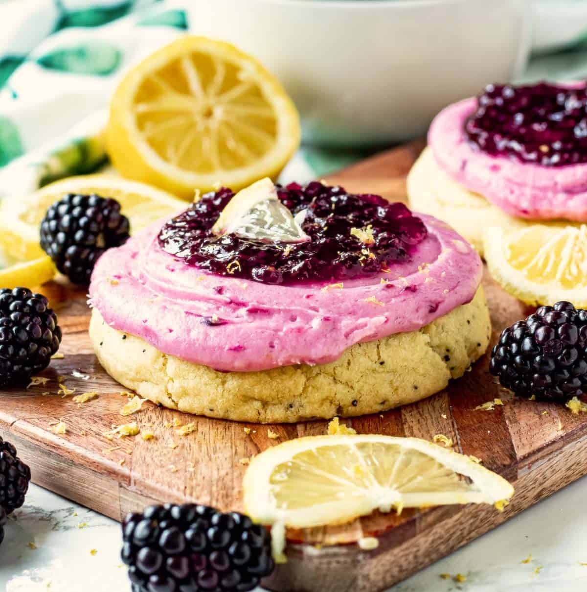 Baked Lemon Blackberry Cookie with frosting on wooden cutting board with lemon slices and blackberries.