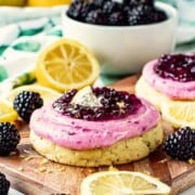 Baked Lemon Blackberry Cookie with frosting on wooden cutting board with lemon slices and blackberries.