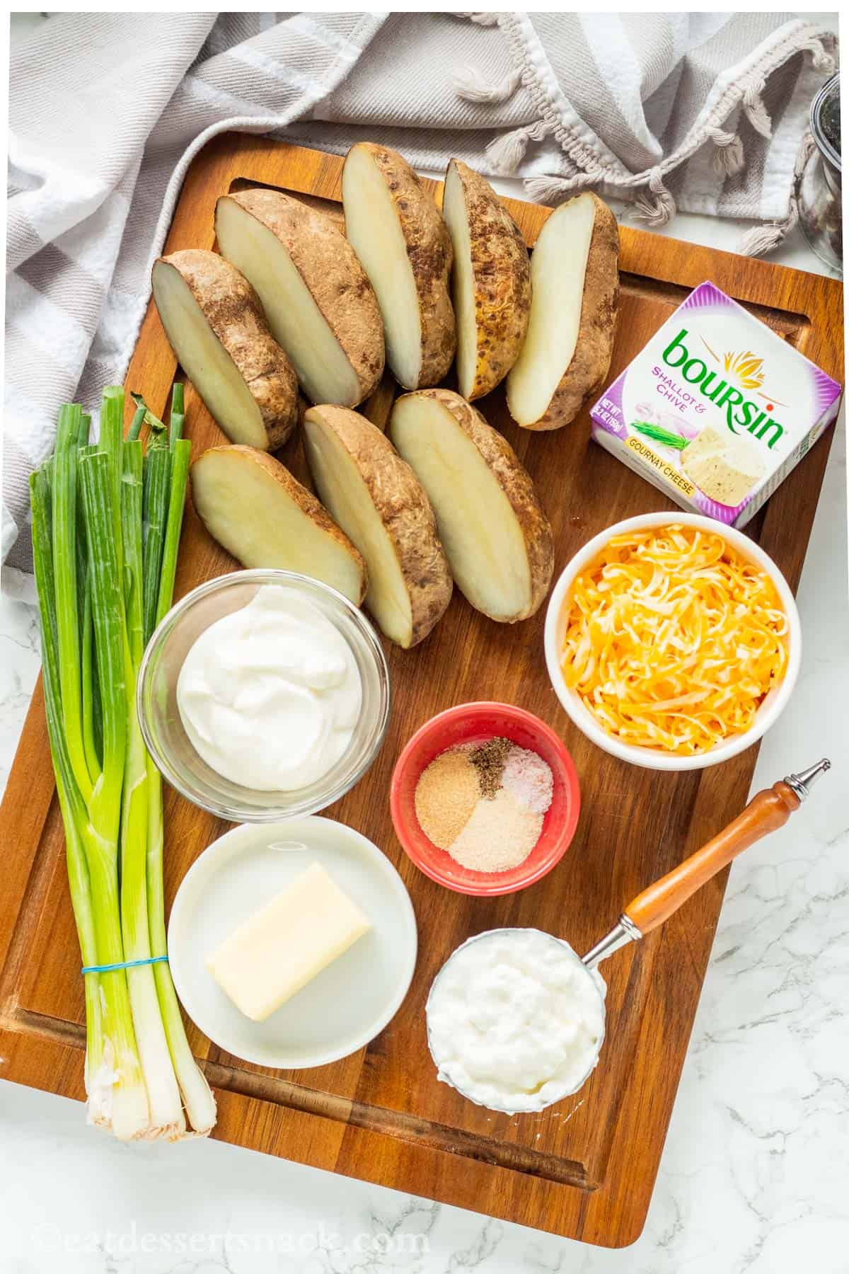 Green onions, sour cream, cottage cheese, cheddar and boursin cheese, potatoes and spices on cutting board.