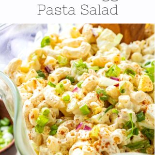 Deviled Egg Pasta Salad in clear glass serving bowl with wooden spoon.