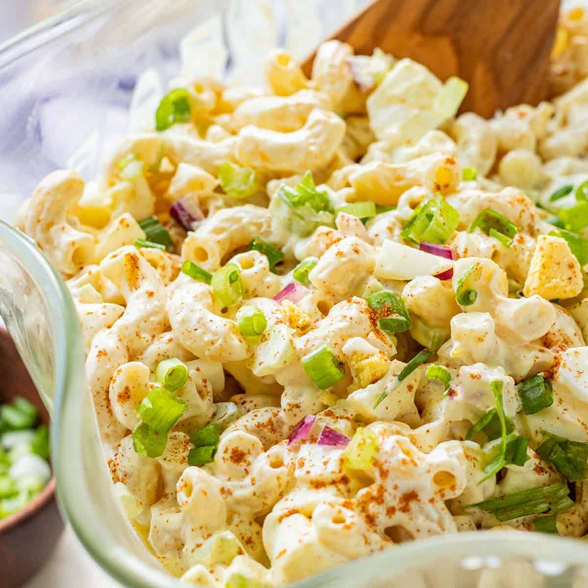 Deviled egg pasta salad in clear glass bowl with wavy edges, paprika and green onions on top.