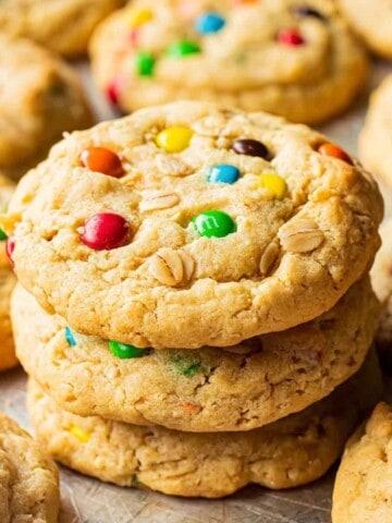 Stack of 3 baked oatmeal m&m cookies on metal baking sheet.