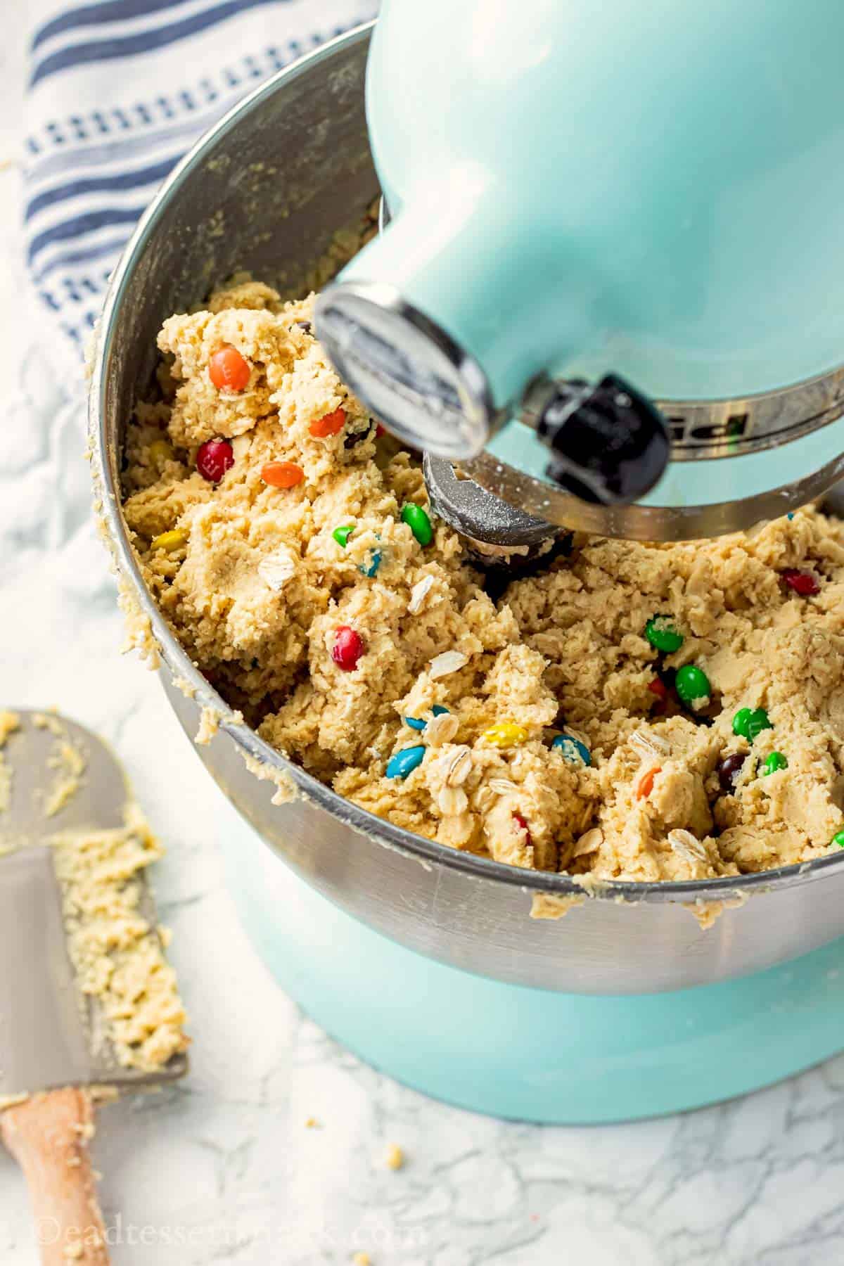 Raw oatmeal M&M cookie dough in metal mixing bowl on blue stand mixer.
