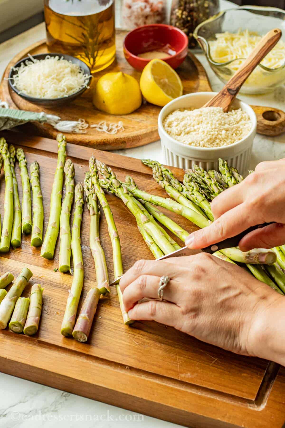 Hands and knife chopping fresh asparagus on wood cutting board.