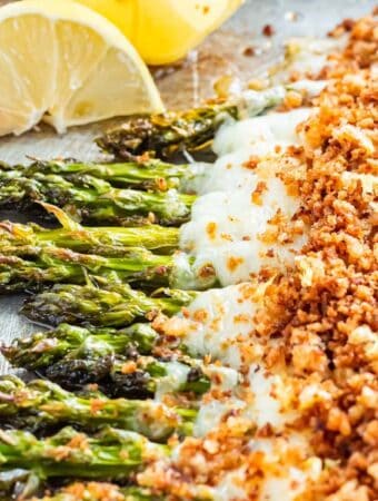 Cheesy baked asparagus on metal pan with lemon wedges.