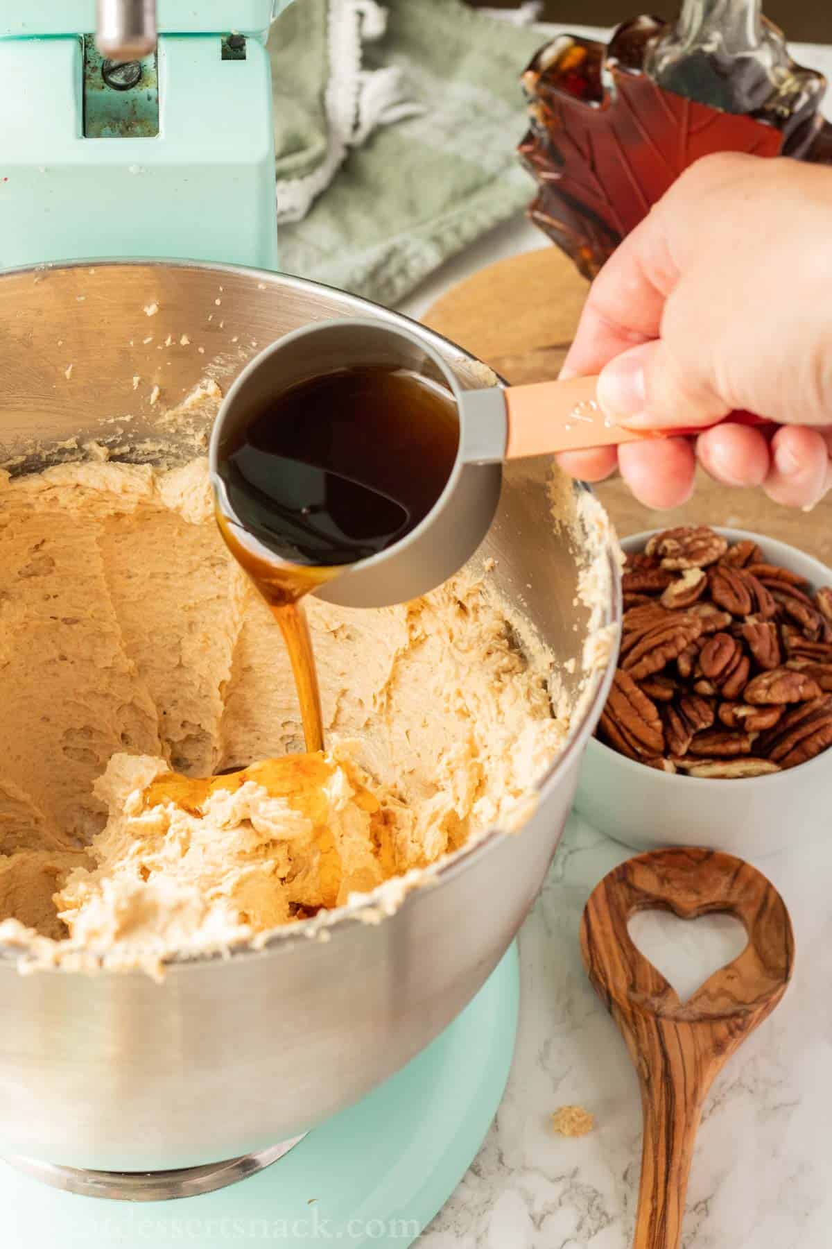 Hand pouring maple syrup into mixing bowl of raw maple cookie dough.