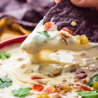 Black chip scooping melted white queso dip out of red bowl.