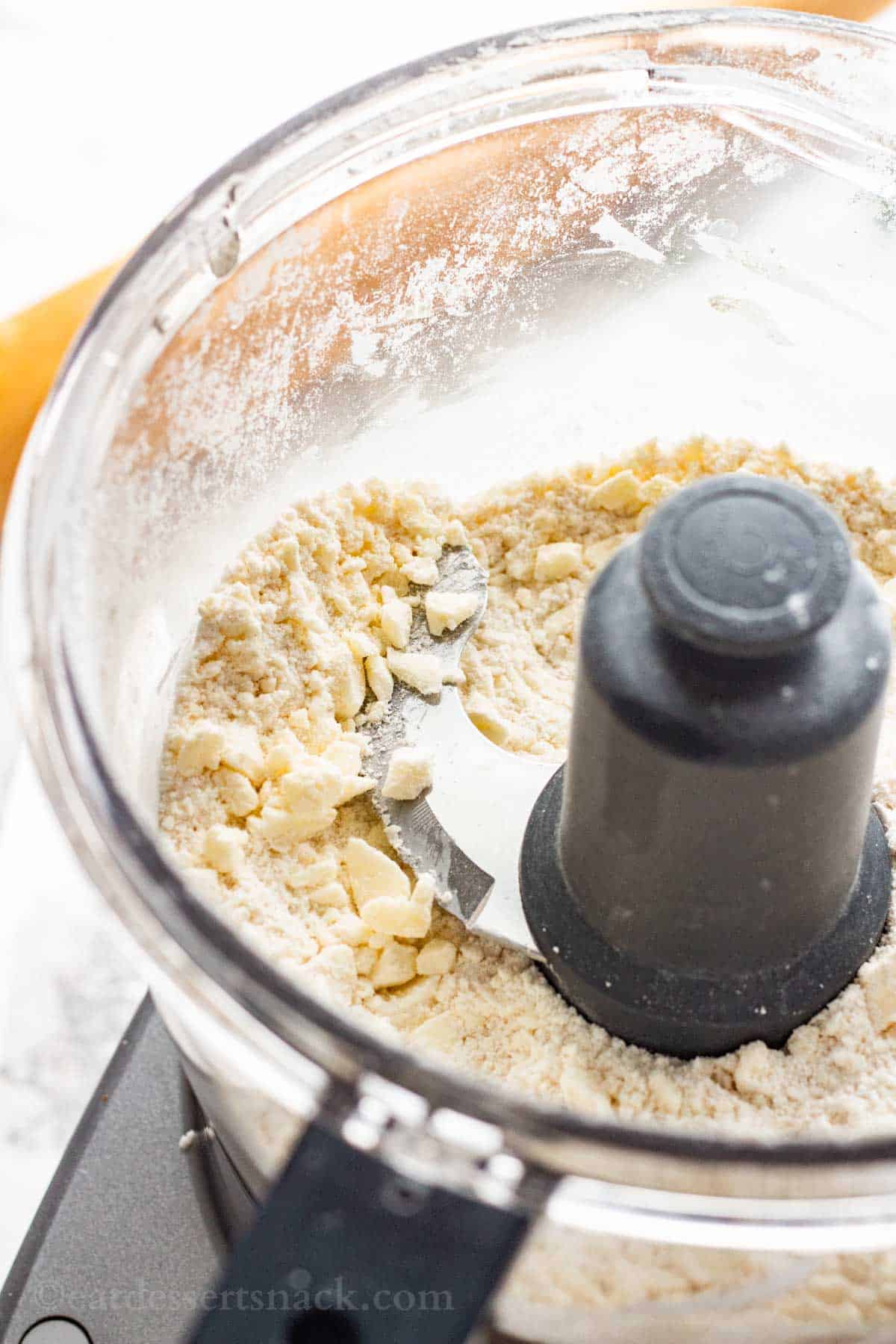 Butter broken in pieces in flour in the bowl of a food processor.