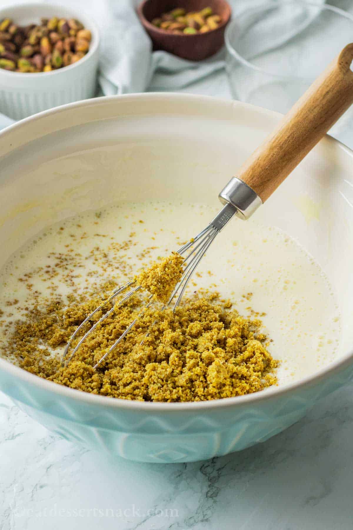 Pouring ground pistachios and sugar into bowl of custard mixture.